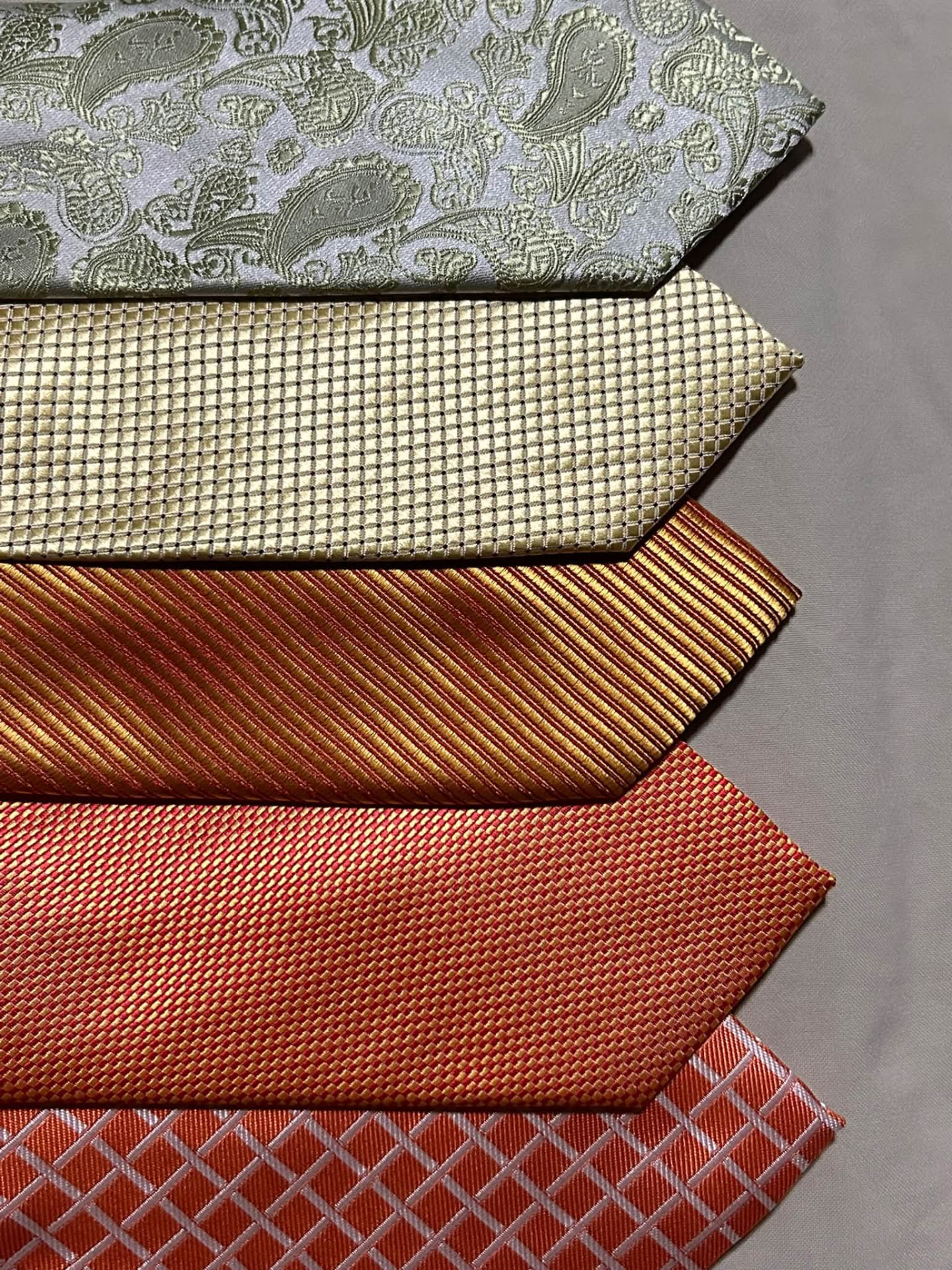 Stack of gold, rust, cream, and sage patterned neckties